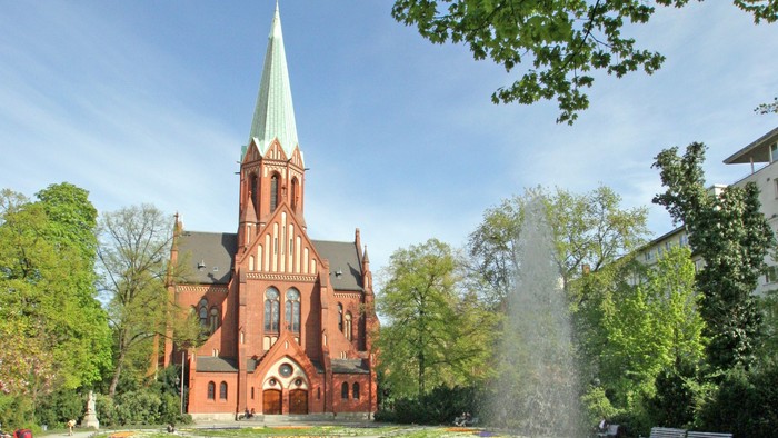 Ein rotes Kirche mit hohem Turm und ein Brunnen im Vordergrund