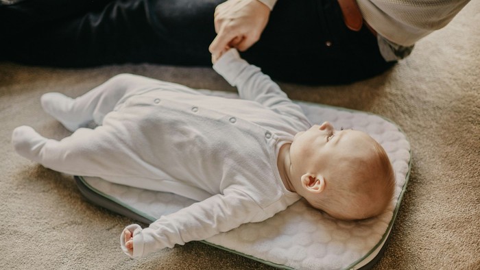 En baby ligger på et puslebord, mens en voksen forsigtigt holder dens hånd.