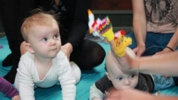 Et spilende barn på gulvet med legetøj og en voksne hånd.