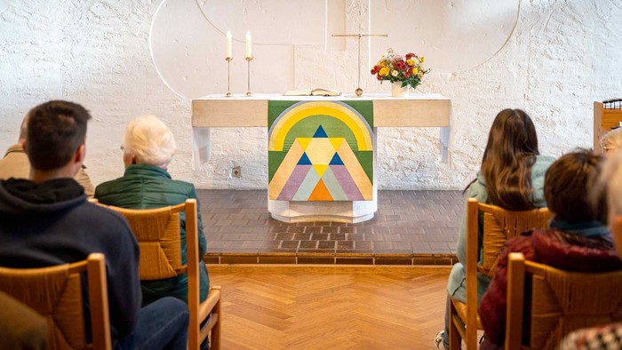 Gemeinde feiert Gottesdienst in Kirche mit farbenfrohem Altar.