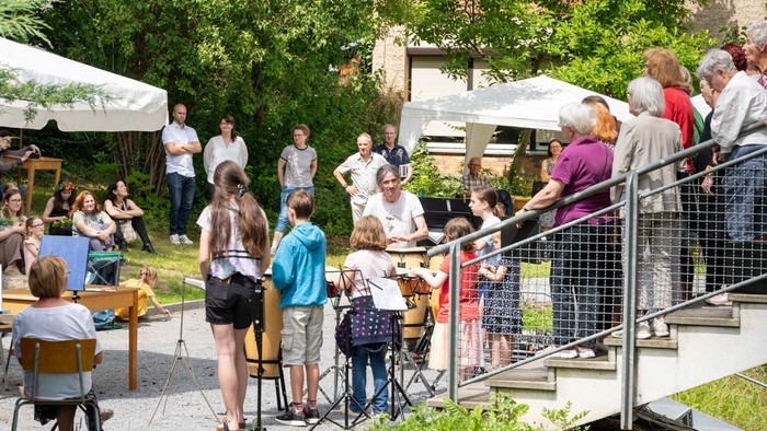Eine Gruppe von Menschen schaut einem Straßenmusiker zu, der auf einem Gehweg spielt.