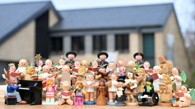 Eine Gruppe von Holzfiguren steht vor einem Haus und singt Weihnachtslieder