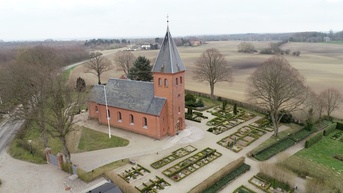 En rød kirke med spiret og omgivelser i landskabet