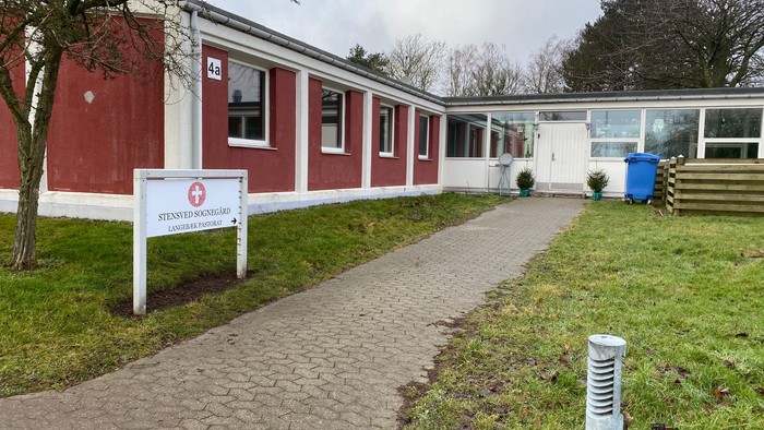 En rød og hvid bygning med et skilt der siger "Røde Kors" og en sti der fører op til den