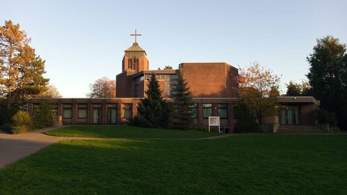 Ein Kirchengebäude mit hohem Turm und grünem Rasen davor