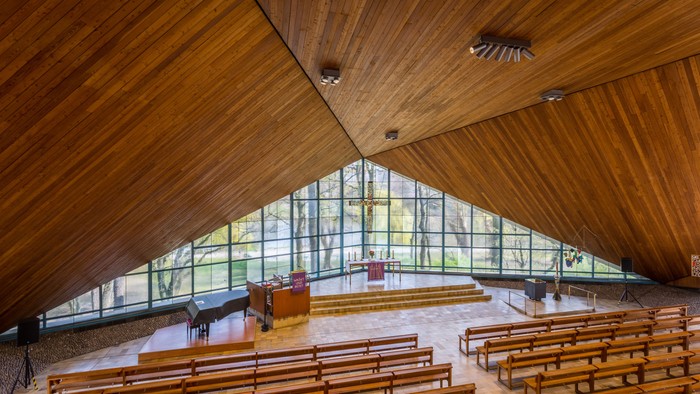 Moderne Kirche mit Holzdecken und großen Fenstern, Holzpulte in Reihen angeordnet