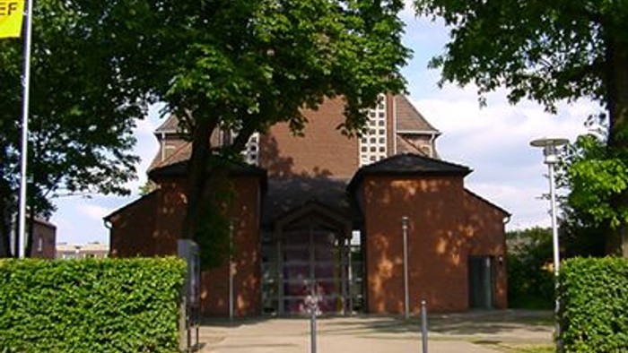 Das Bild zeigt eine Kirche mit hohem Turm, umgeben von Bäumen und Büschen.