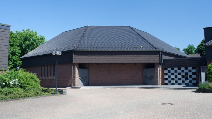 Das Bild zeigt ein modernes Gebäude mit schwarzem Dach und einem gepflasterten Vorplatz.