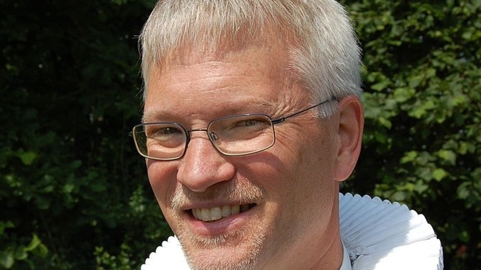 Mand med hvid krage og briller.