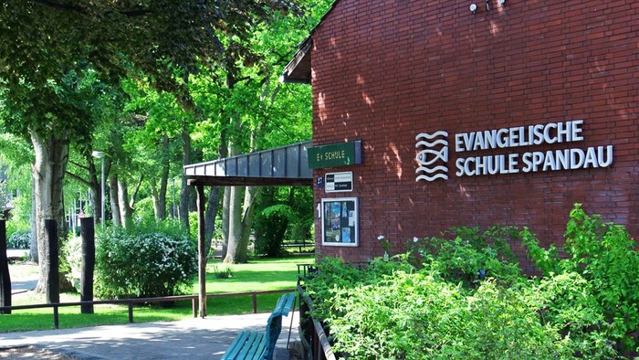 Das Bild zeigt den Eingang zur Evangelischen Schule Spandau mit einem Schild und einem Weg durch den Park.