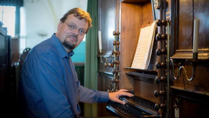 Mann spielt Klavier in einem Raum mit großen Fenstern.