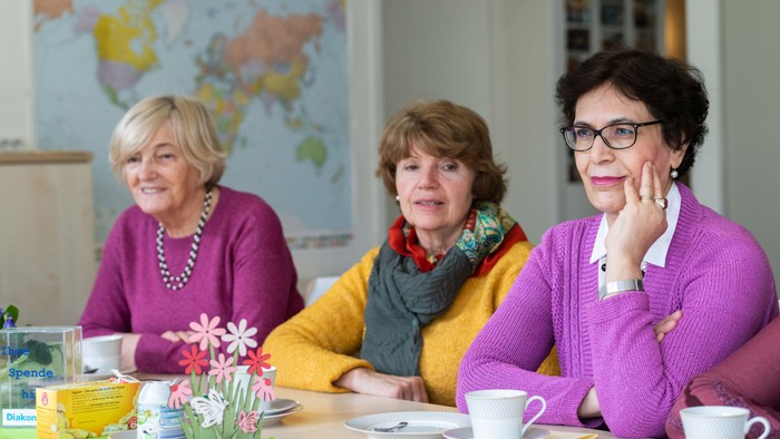 Drei ältere Frauen sitzen an einem Frühstückstisch und unterhalten sich.