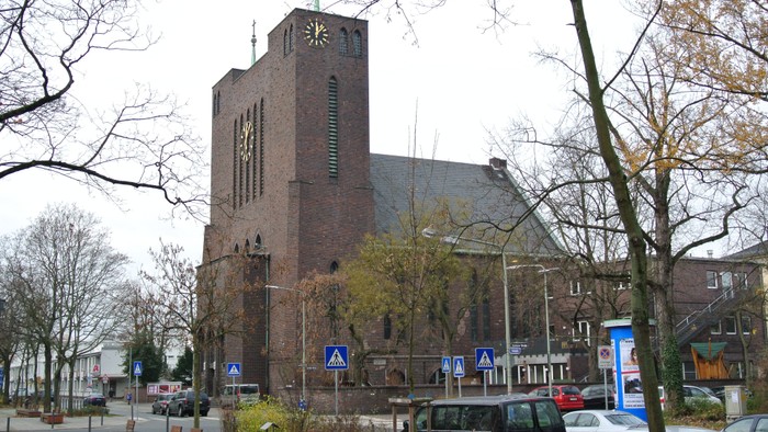 Große Ziegelkirche mit hohem Turm und mehreren Autos davor