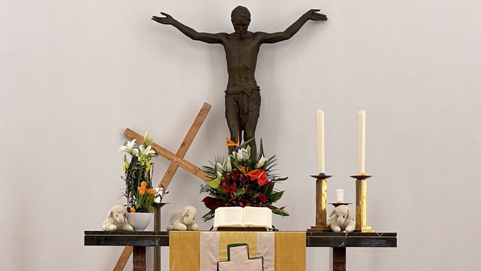 Ein feierlicher Altar mit einer Kruzifix-Statue, Blumenschmuck, Kerzen und einem Kreuz auf einer hölzernen Plattform.
