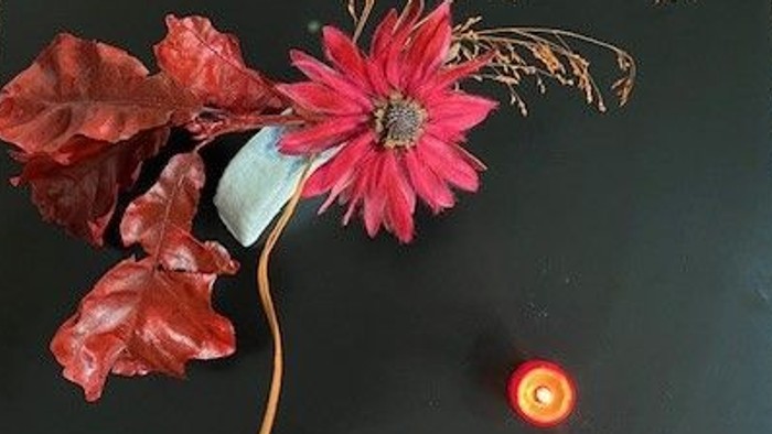 Ein schwarzer Tisch mit einer pinken Blume und Herbstblättern.