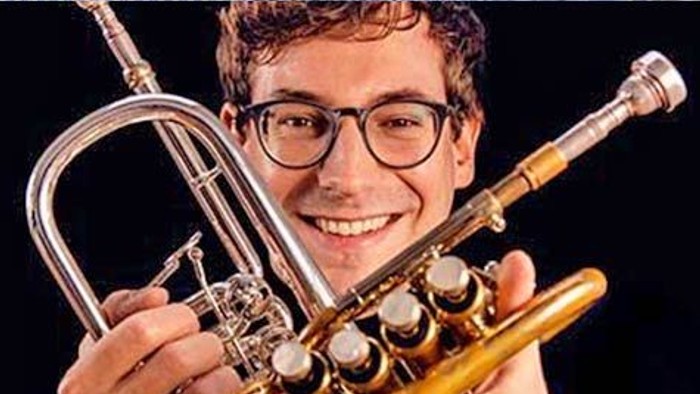 Ein Mann mit Brille hält eine Trompete und lächelt