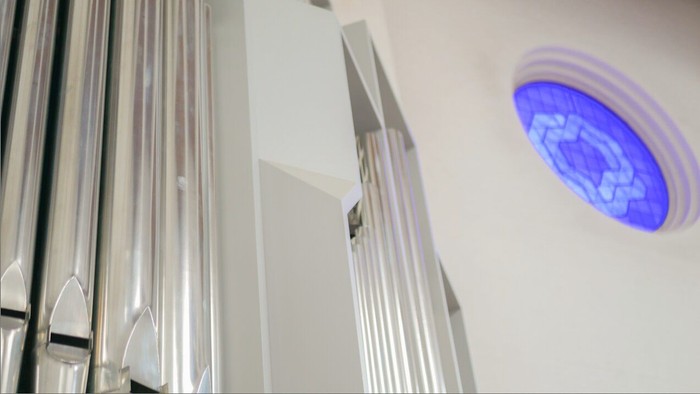 Moderne elevator med oplyst cirkulært skilt, der viser et stiliseret logo, og metalliske lodrette paneler.