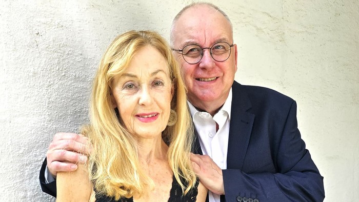 Ein Mann und eine Frau stehen Arm in Arm vor einer weißen Wand.