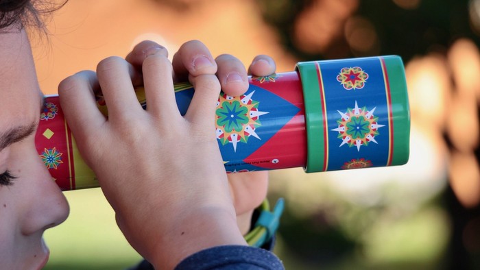 Ein Kind hält ein buntes Spielzeugteleskop vor das Auge.