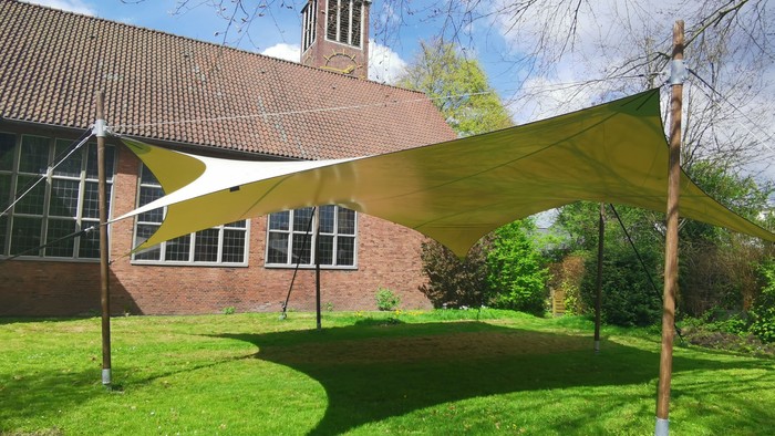 Ein großes gelbes Zelt auf einem grünen Rasen vor einem Backsteingebäude mit einem Kirchturm.