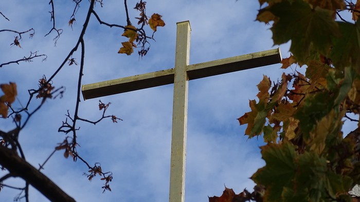 Ein hölzernes Kreuz vor Herbstblättern und blauem Himmel