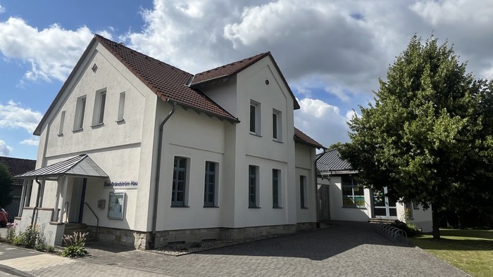 Das Bild zeigt das Laggenbecker Gemeindehaus, ein weiß verputztes Gebäude mit einem Anbau rechts.