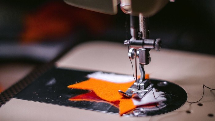 Eine Nähmaschine näht orange und rote Stoffstücke auf einem weißen Stoff.