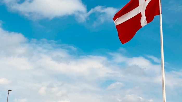 En rød flag med hvidt kors foran en folkemængde under et blømt skyoverskyd