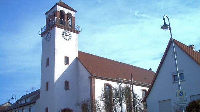 Weiße Kirche mit hohem Turm und Uhr, rote Ziegeldächer, klarer blauer Himmel