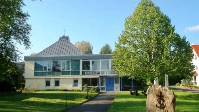 Modernes Haus mit großen Fenstern, umgeben von Bäumen und Rasen.