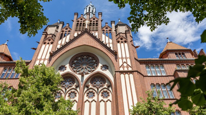 Gothische Architektur mit großen Fensterbogen und Türmen, umgeben von Bäumen