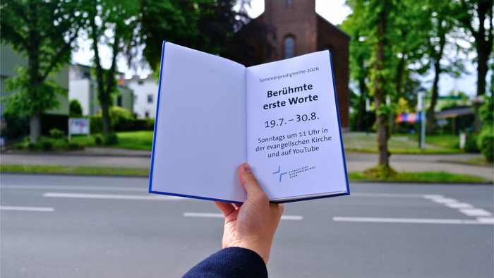 Eine Hand hält ein offenes Buch, das für eine bekannte Literaturveranstaltung vom 19. Juli bis 30. August in einer Kirche wirbt.
