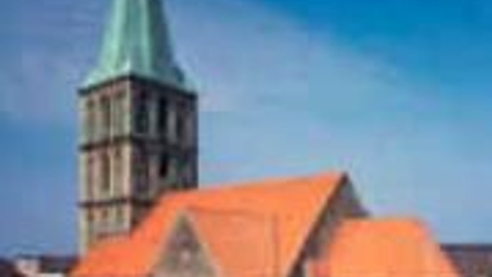 Kirche mit hohem Kirchturm und rotem Dach vor blauem Himmel.