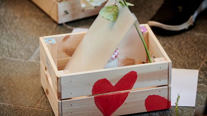 Ein Holzkasten mit Herzdekoration und einer Blume darin