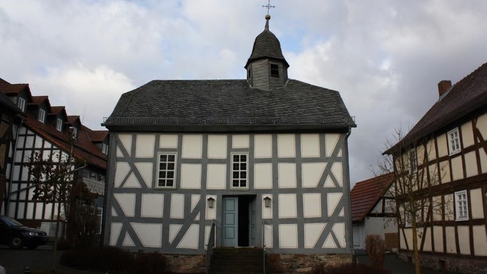 Schwarz-weißes Fachwerkgebäude mit einem kleinen Turm und einer Wetterfahne.