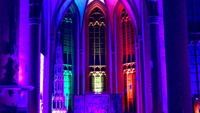 Kircheninneres mit farbenfroher Beleuchtung und bunten Bleiglasfenstern.