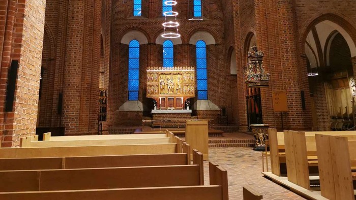 Elegant kirkeinteriør med træbænke, farvede glasvinduer og et detaljeret alter med religiøse statuer.