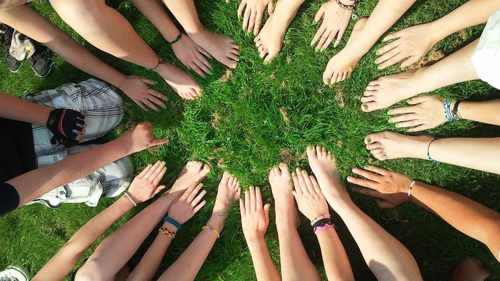 Ein Kreis von Händen auf Gras, symbolisch für Einheit und Zusammenhalt