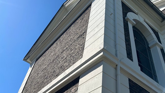 Weißes Gebäude mit grauen Steinen und weißen Fensterrahmen unter blauem Himmel