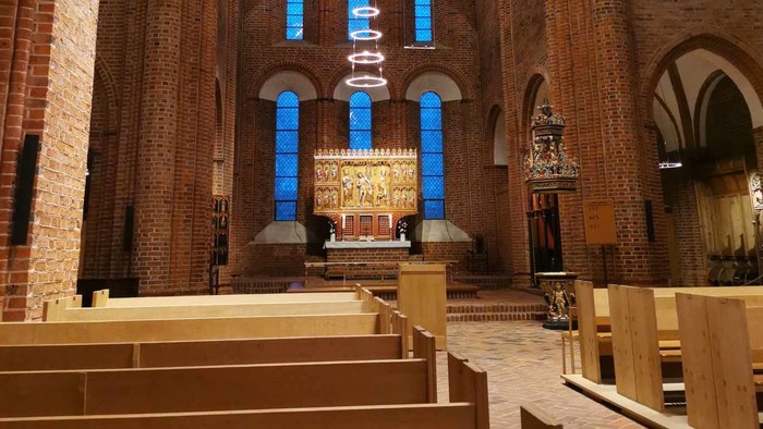 Elegant kirkeinteriør med træbænke, farvede glasvinduer og et detaljeret alter med religiøse statuer.
