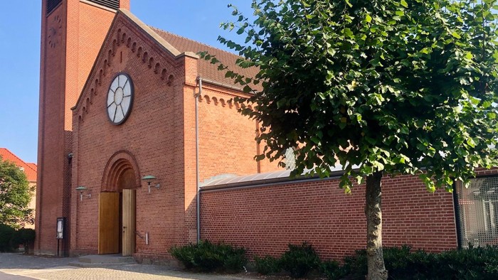 Røde murstenskirke med klokke og træ foran
