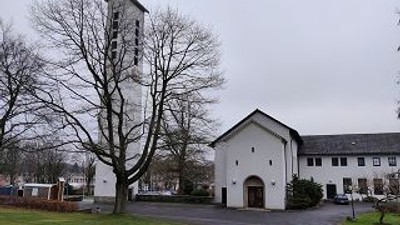 Ein weißes Gebäude mit Turm und parkenden Autos davor.