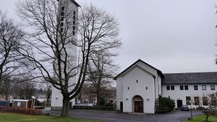 Ein weißes Gebäude mit Turm und parkenden Autos davor.