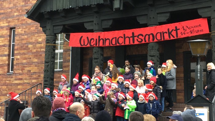 Menschenmenge vor Holzhaus mit Weihnachtsmarkt-Schild