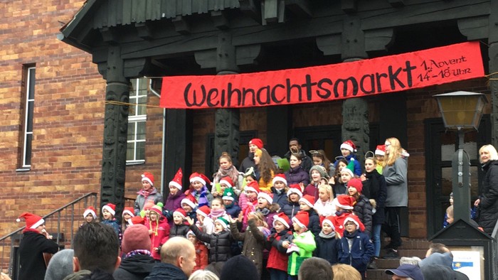 Menschenmenge vor Holzhaus mit Weihnachtsmarkt-Schild
