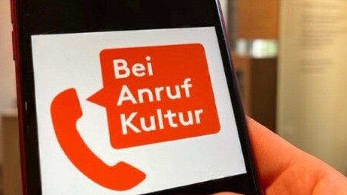 Hand hält Smartphone mit "Bei Anruf Kultur" App.