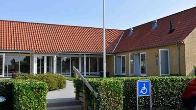 En rødtaget hus med trappe og handicapparkeringstegn.