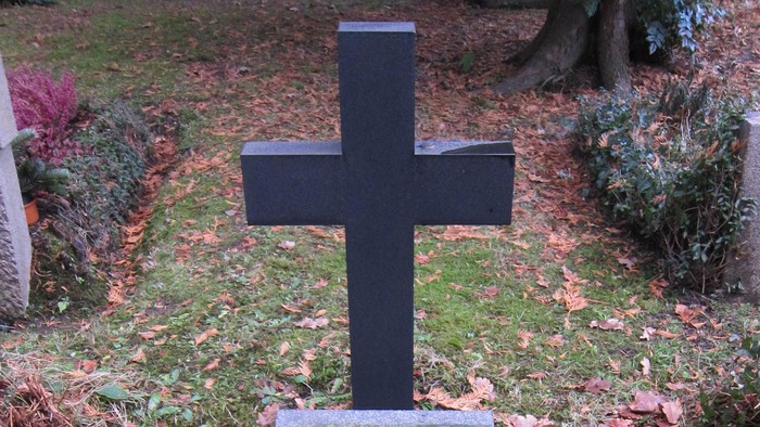 Ein schwarzes Kreuz auf einem Grabstein in einem Friedhof.