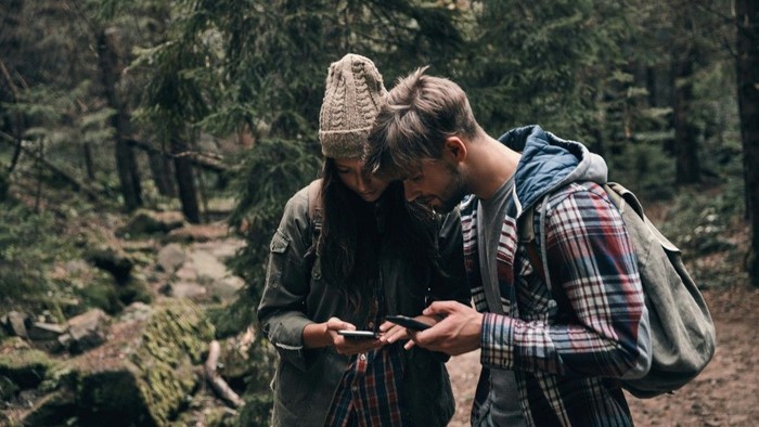 Zwei junge Menschen auf der Wanderung suchen in ihren Handys nach dem richtigen Weg.