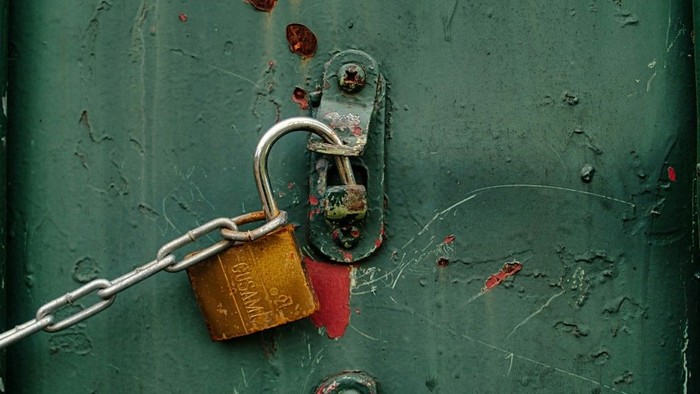 Ein Schloss an einer Kette ist offen und ein Tür lasst sich entriegeln